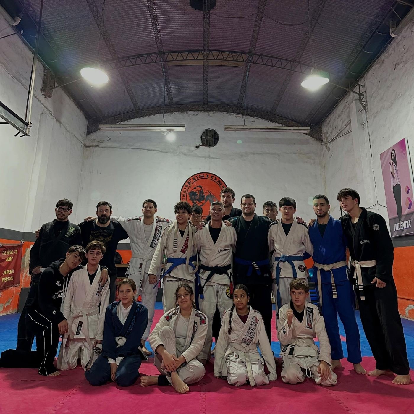 Alumnos y profesores de Fusion posando juntos sobre el tatami, con el logo del gimnasio en la pared
